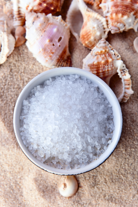 Small bowl of epsom salts with seashells on a sandy background These epsom salts will be used to make DIY bath soaks