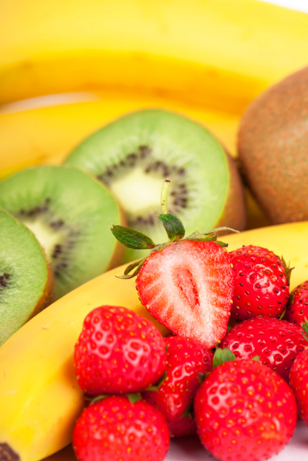 A selection of fresh fruits including bananas, kiwi slices, strawberries, and a mango, arranged on a surface used to depict candle fragrance oil