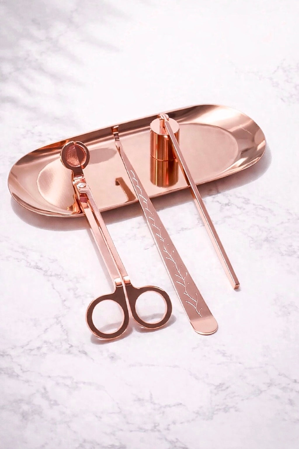 Rose gold candle tool set on a white marble surface