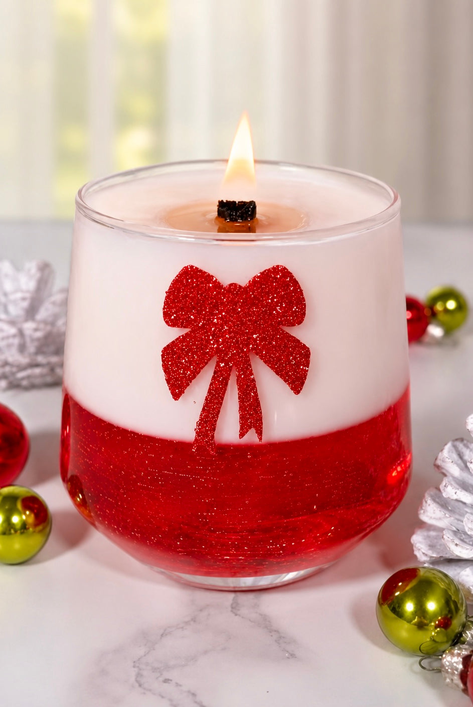 Decorative candle with a red bow design on a marble surface with Christmas ornaments.