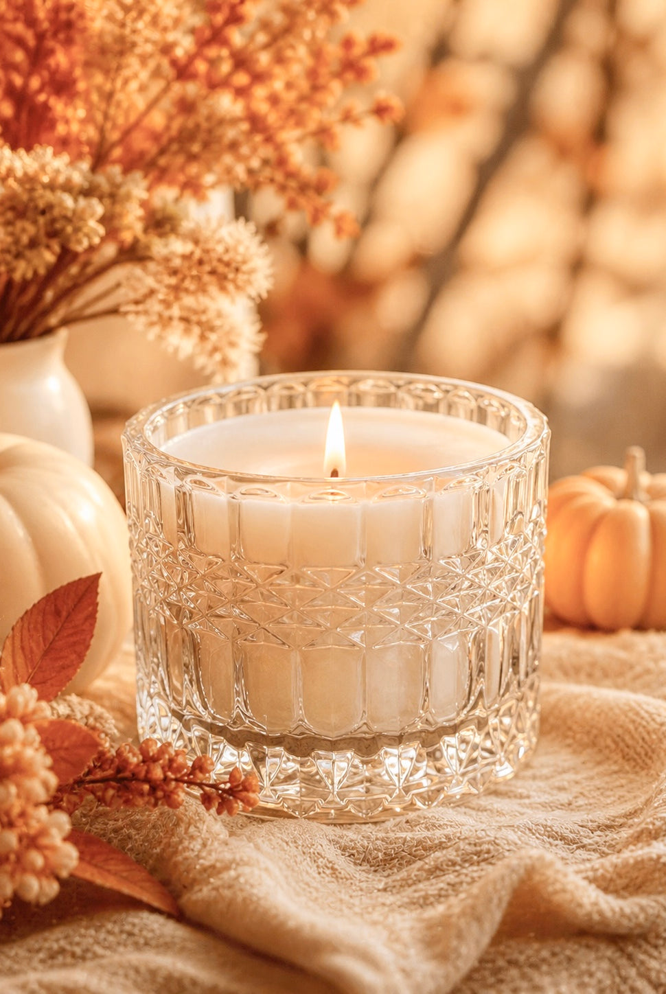 Candle in a decorative lush crystal clear glass vessel with pumpkins and foliage on a soft background