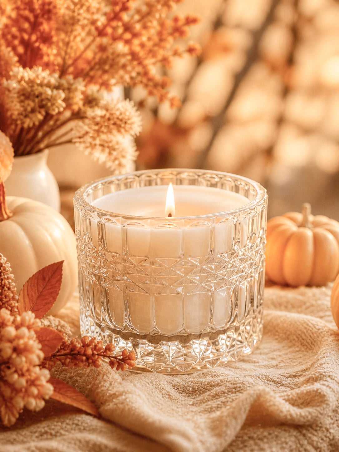 Candle in a decorative lush crystal clear glass vessel with pumpkins and foliage on a soft background