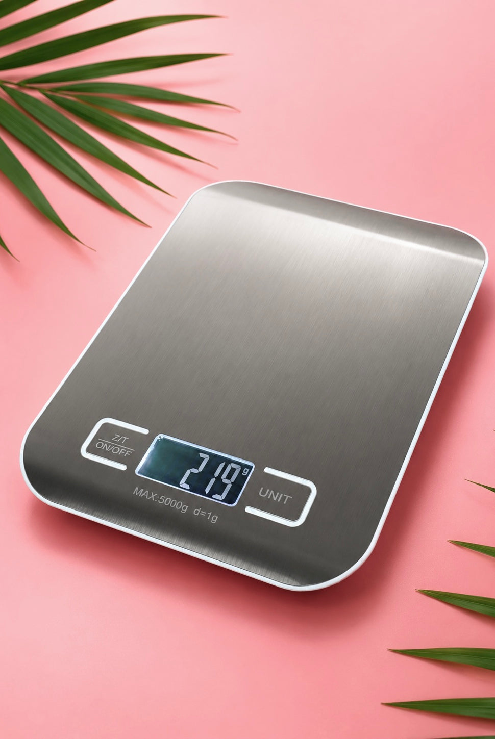 Digital kitchen scale on a pink background with green leaves