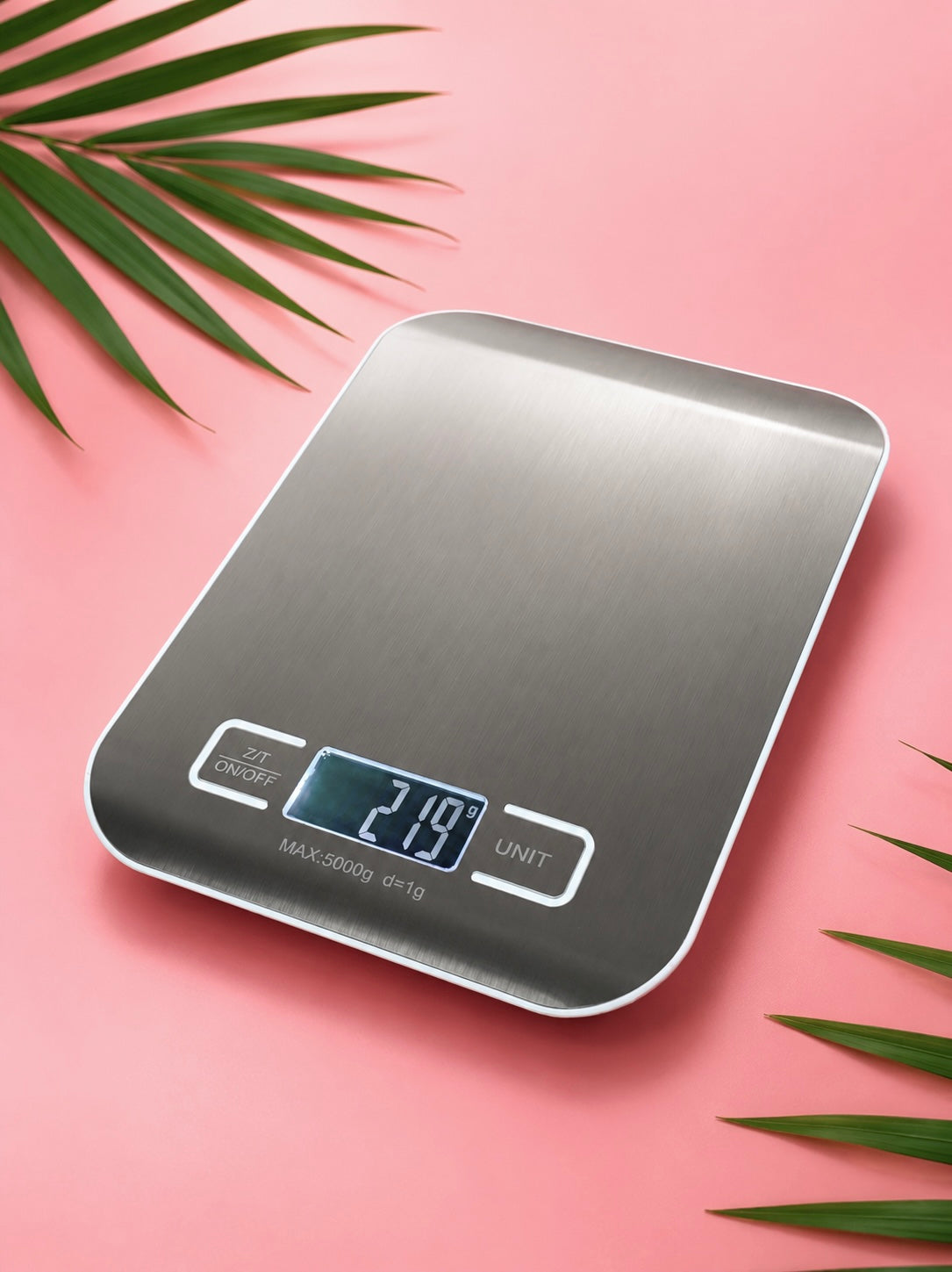 Digital kitchen scale on a pink background with green leaves