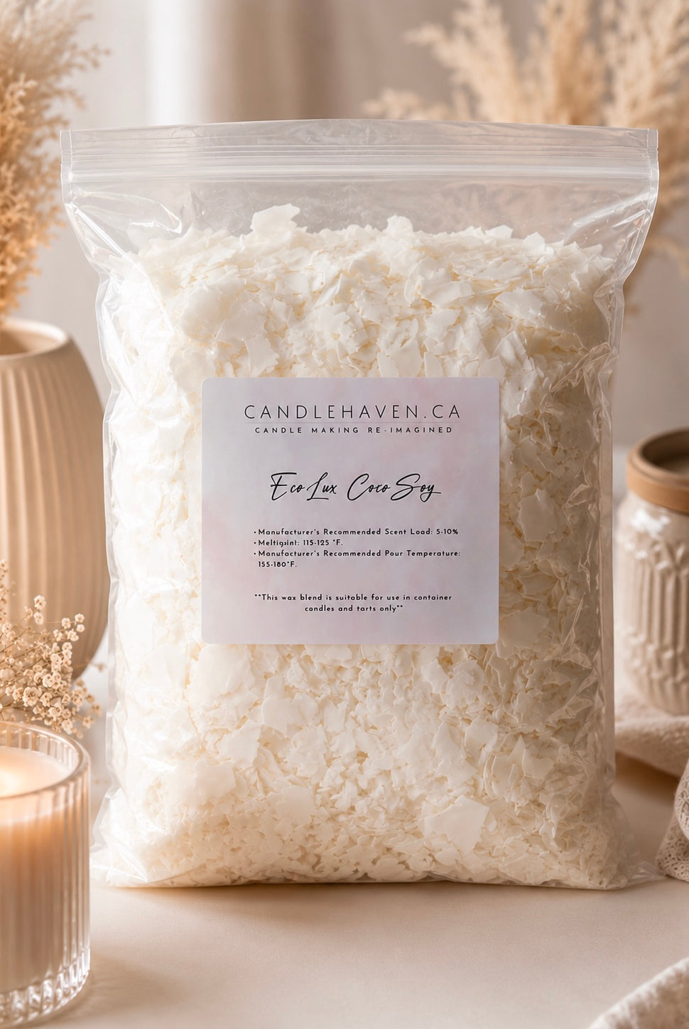 A clear plastic bag filled with white wax flakes, labelled EcoLux Coco Soy Wax by Candlehaven.ca, styled on a tabletop with a lit candle, dried flowers, and ceramic jars.