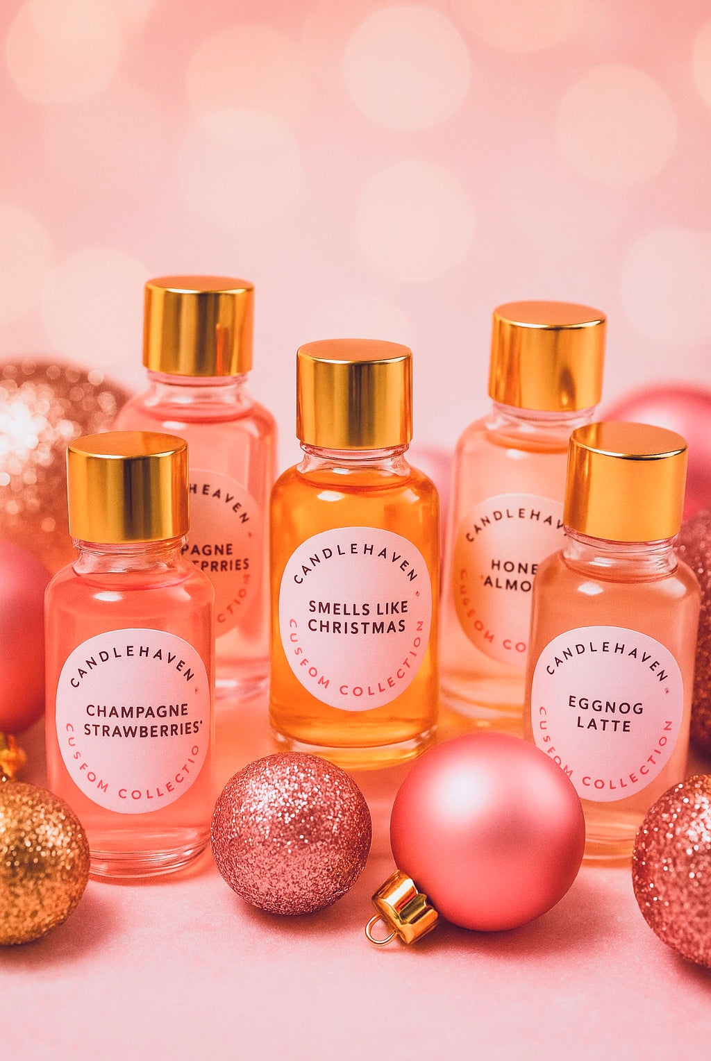 Best Christmas Fragrance Oils Canada | Set of small bottles that are the Holiday Fragrance Oil Collection from Candlehaven.ca on a pink background with Christmas ornaments.