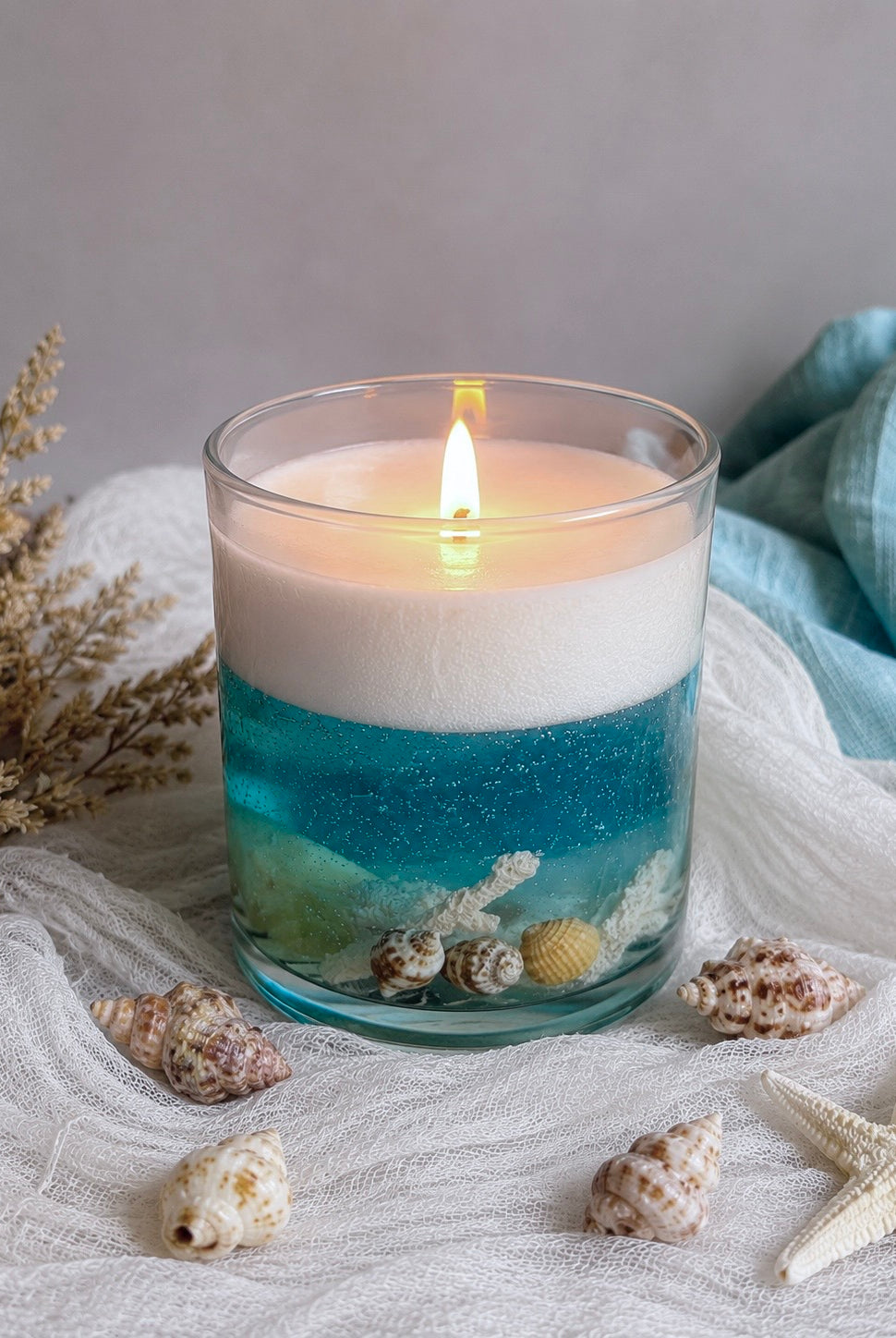 Candle in a Ilite vessel with blue and white layers, surrounded by shells and starfish on a textured surface.