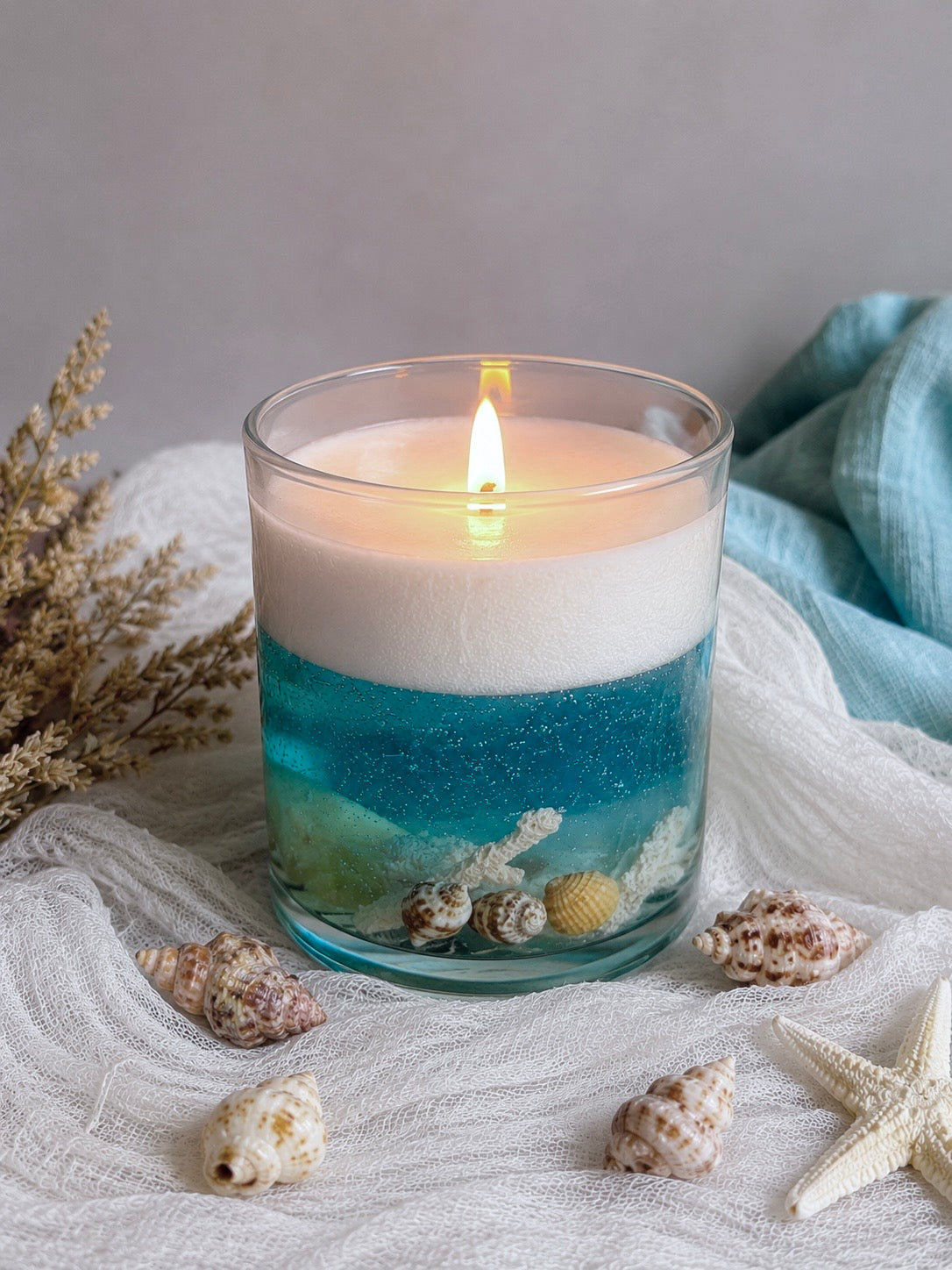 Candle in a Ilite vessel with blue and white layers, surrounded by shells and starfish on a textured surface.