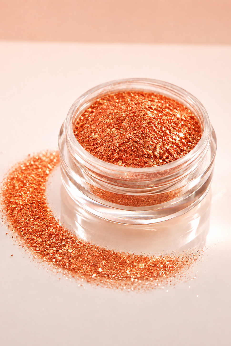 Shimmering orange diamond sparkle dust in a small clear round jar, with some of the diamond sparkle dust spilled in a curved line beside it on a soft light beige background.