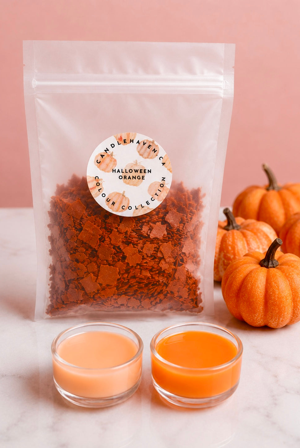 Wax dye chips in a clear pouch labelled “Halloween Orange” with two clear plastic cups into shades of orange that this product can achieve. Pumpkins decorate the background.
