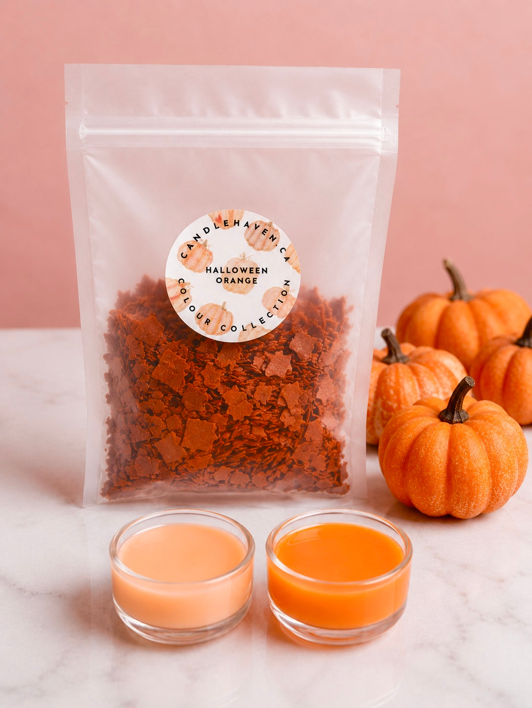 Wax dye chips in a clear pouch labelled “Halloween Orange” with two clear plastic cups into shades of orange that this product can achieve. Pumpkins decorate the background.