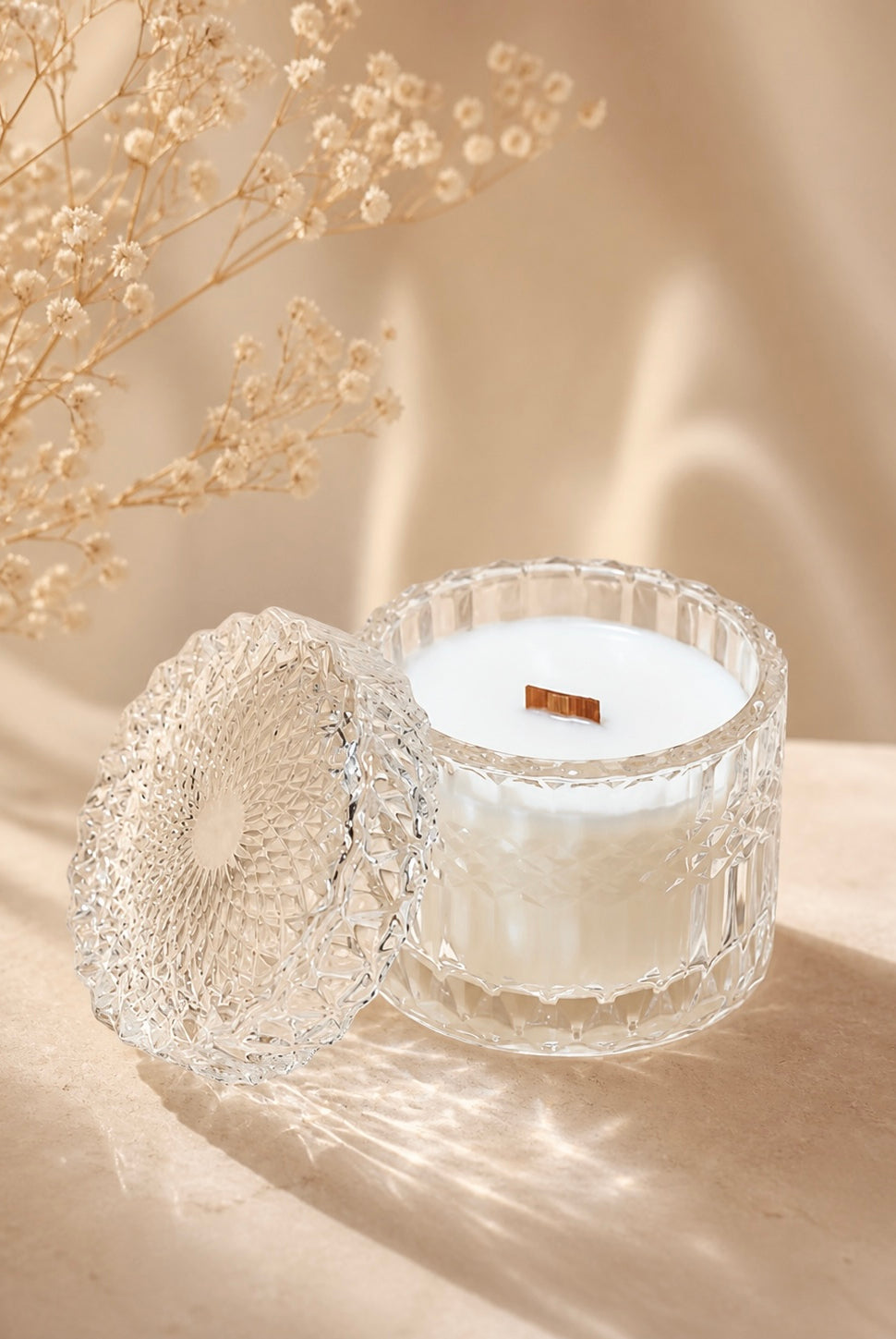 Clear vessel with lid with wax and wood wick inside on a light background