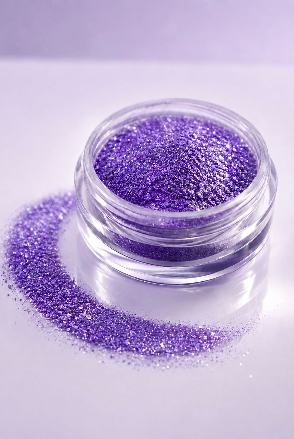 A small clear round jar filled with sparkling purple diamond sparkle dust, with additional loose purple diamond sparkle dust spilled in a curved line beside it on a pale lavender background.