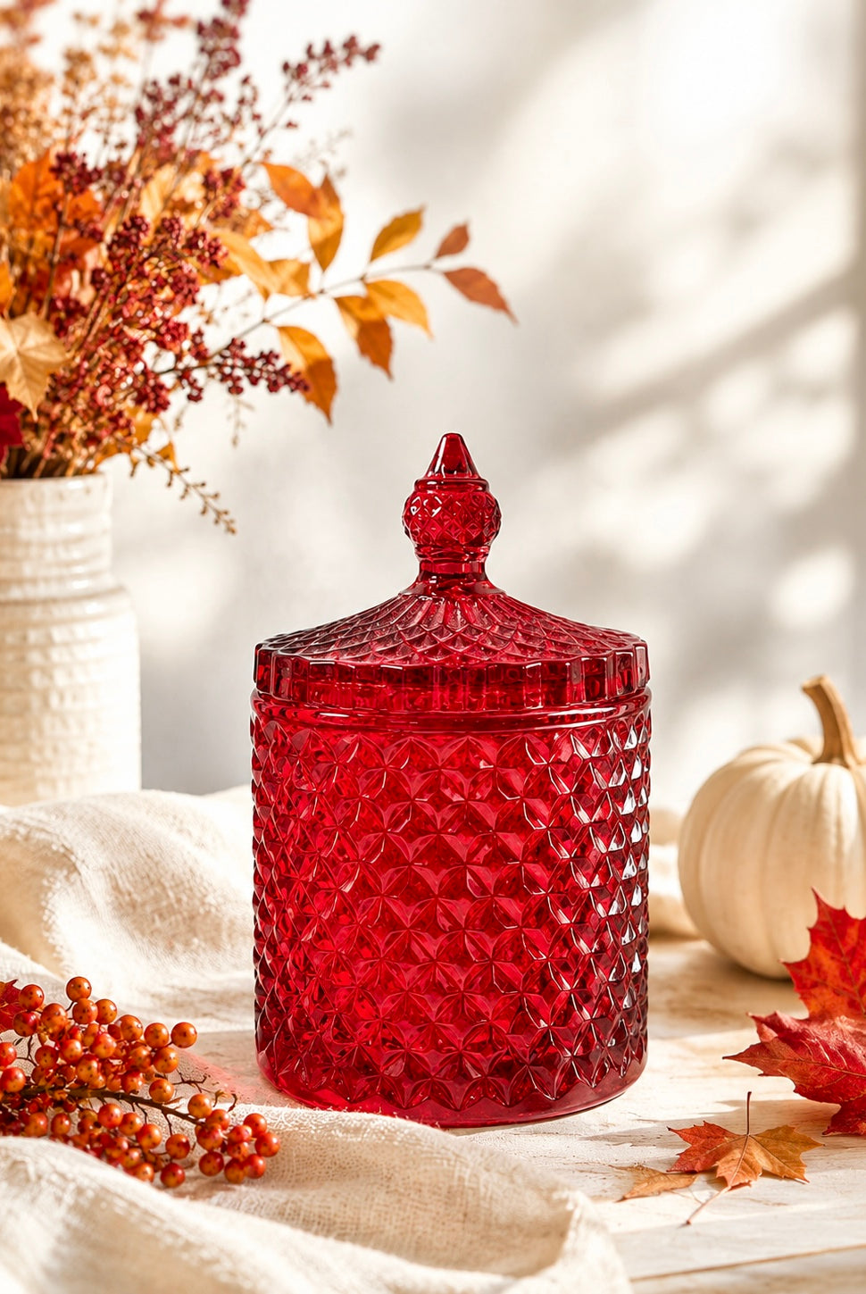 Red glass geocut jar used for candle making with lid on a surface with autumn decorations