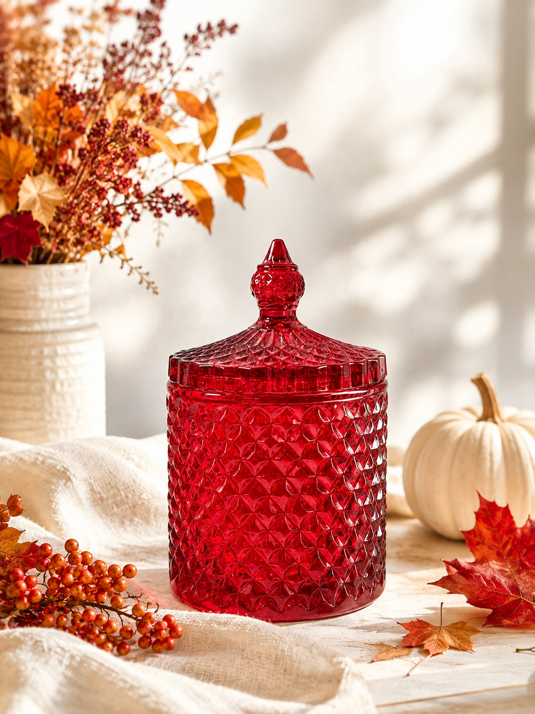 Red glass geocut jar used for candle making with lid on a surface with autumn decorations