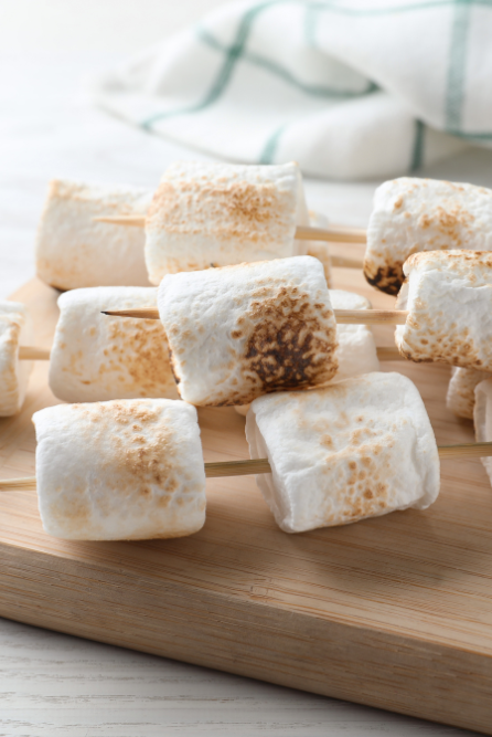 Roasted Marshmallows on skewers with grill marks on a wooden board representing roasted marshmallow fragrance oil for candle making
