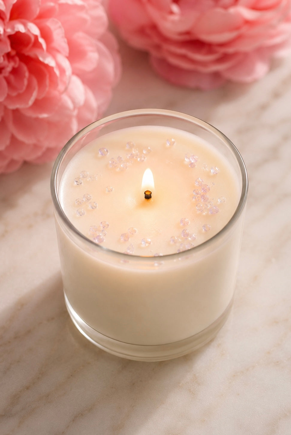 A white candle with rose mini chips on top on a light background with pink flowers