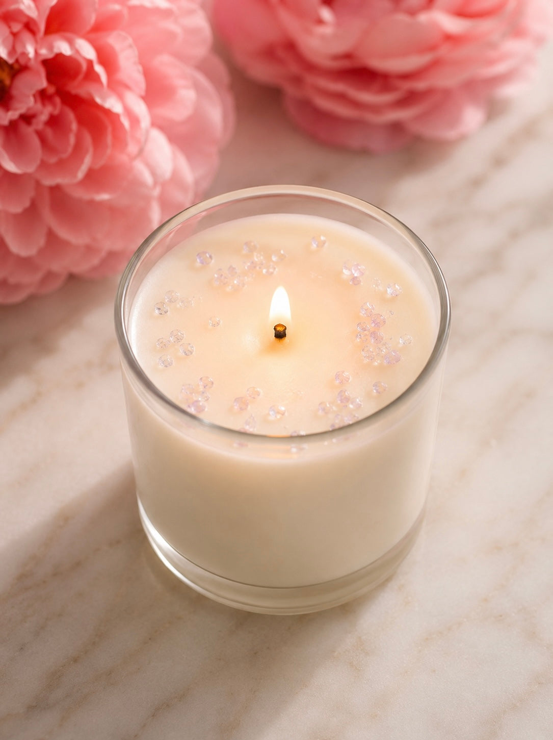 A white candle with rose mini chips on top on a light background with pink flowers