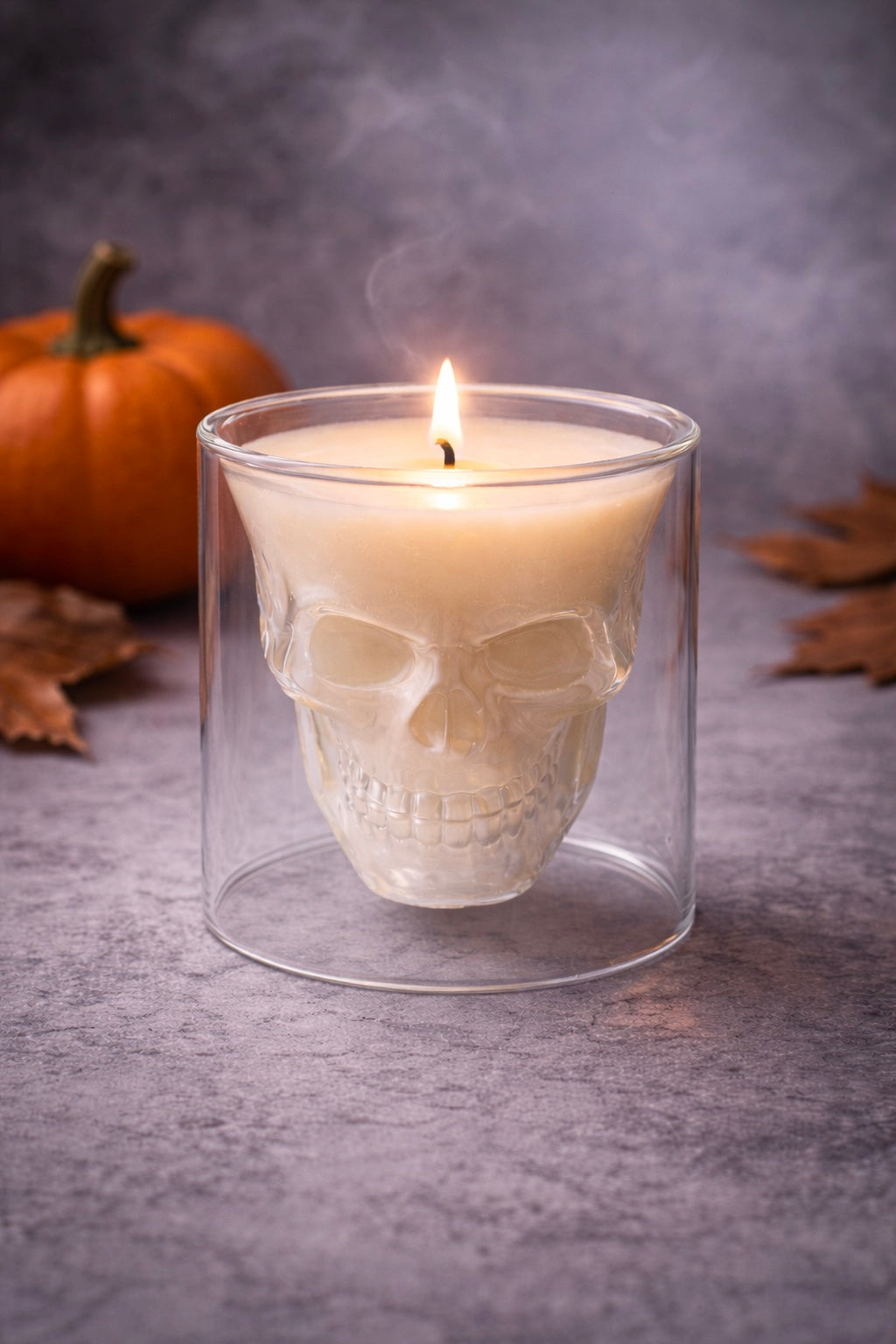 Skull-shaped candle in a Skully double walled glass holder with a pumpkin and leaves in the background