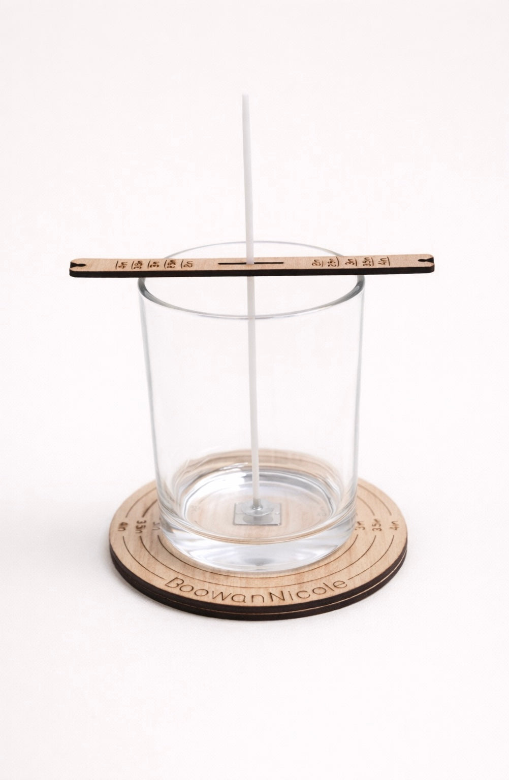 Clear glass candle jar sitting on a wooden wick centering tool on a white background