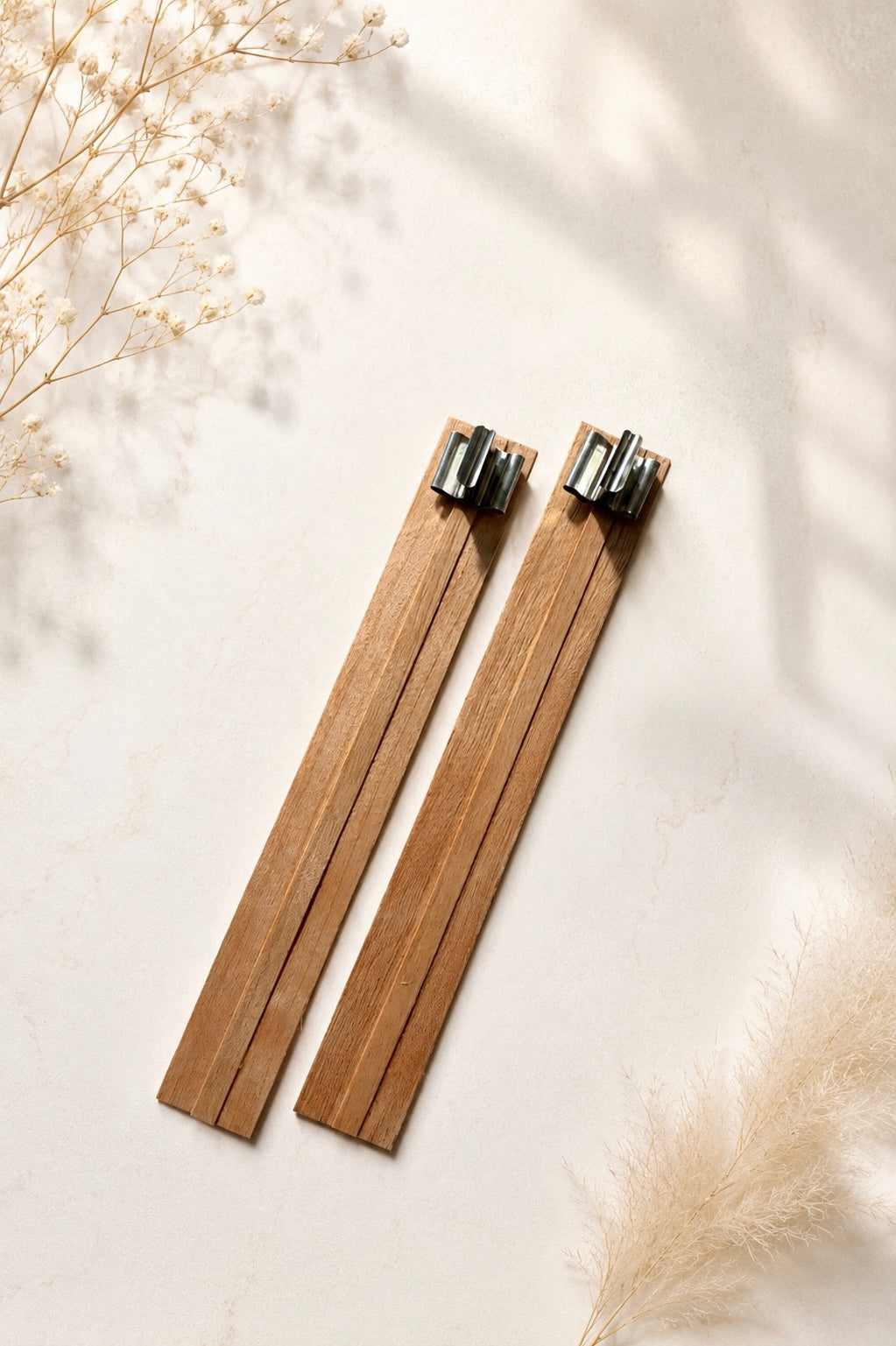 Two wooden wicks for candle making with metal wick clips on a light background with dried baby’s breath