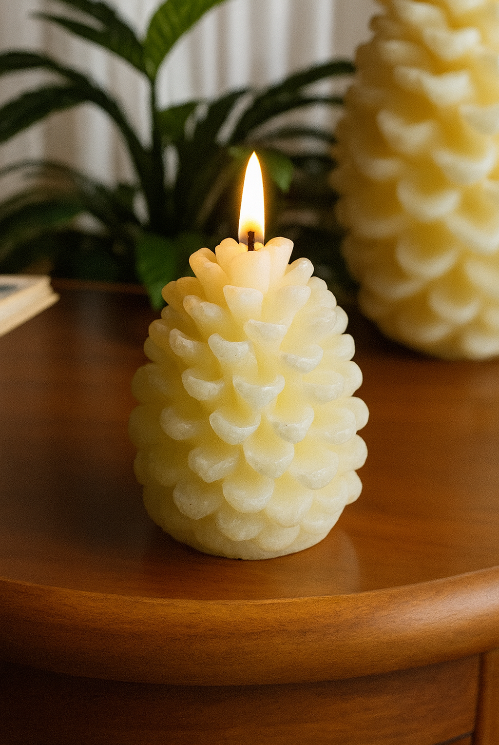 Pinecone candle with a lit wick on a wooden surface, with another similar candle in the background pinecone silicone mold used in candle making in Canada