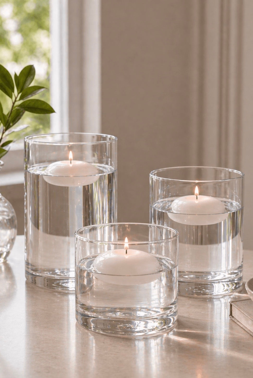 Three glass candle holders with floating candles on a reflective surface.