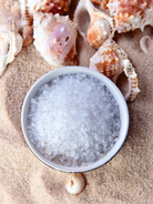Small bowl of epsom salts with seashells on a sandy background These epsom salts will be used to make DIY bath soaks