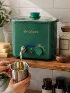 Green ToAuto wax melter with a person pouring liquid into a metal cup on a wooden surface.