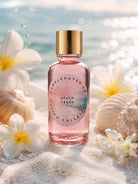 Pink bottle of Candle Haven Beach Tease fragrance oil for candle making on sand with flowers and shells