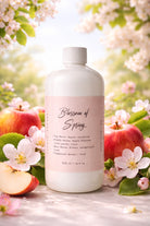 Bottle of 'Blossom of Spring' 500ml candle fragrance oil by Candlehaven.ca with apples and flowers in the background