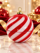 A glossy Christmas ornament shaped like a candy cane, featuring diagonal red and white stripes with a gold cap and hanging loop, set on a marble surface with festive red and gold holiday decorations blurred in the background.