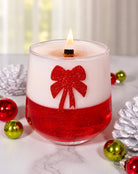 Decorative candle with a red bow design on a marble surface with Christmas ornaments.