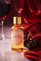 Bottle of Candlehaven’s ‘Midnight Cherry Merlot' candle fragrance oil with cherries and a glass of wine on a red fabric background