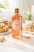 Bottle of 'Cinnamon Swirl' fragrance oil on a surface with cinnamon rolls in the background