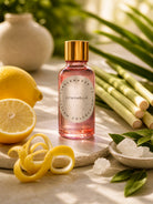 Pink bottle of citronella fragrance oil for candle making with lemon peel and lemon grass and camphor in the background 