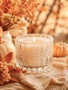 Candle in a decorative lush crystal clear glass vessel with pumpkins and foliage on a soft background