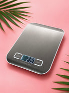 Digital kitchen scale on a pink background with green leaves