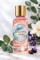 Pink bottle with gold cap labeled 'Eucalyptus Noir' by Candlehaven on a marble surface with greenery and flowers.