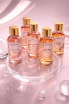 Collection of fall themed fragrance oil bottles on a reflective surface with a pink gradient background