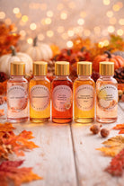 Set of five small bottles with gold caps on a wooden surface with autumn leaves and pumpkins in the background.