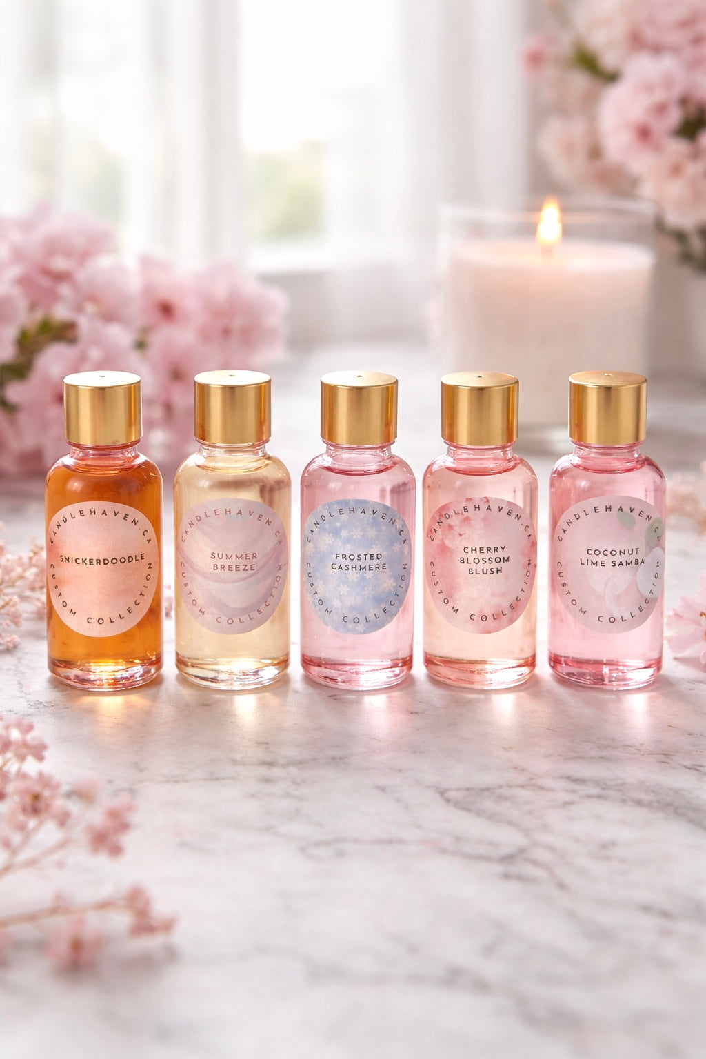 Five small bottles of candle fragrance oils with gold caps on a marble surface, surrounded by flowers and a candle.