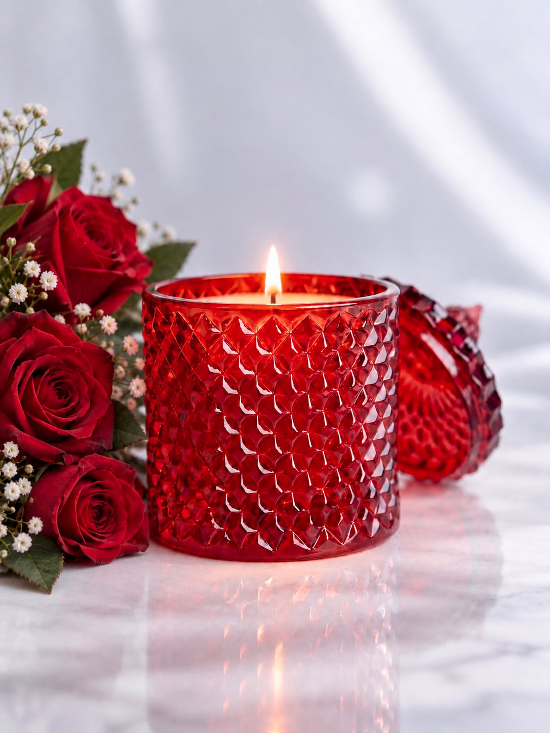 Red candle vessel with lid made from geo cut glass on a light background with roses and baby’s breath in the background 