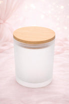 Frosted glass candle jar with a wooden lid on a pink background