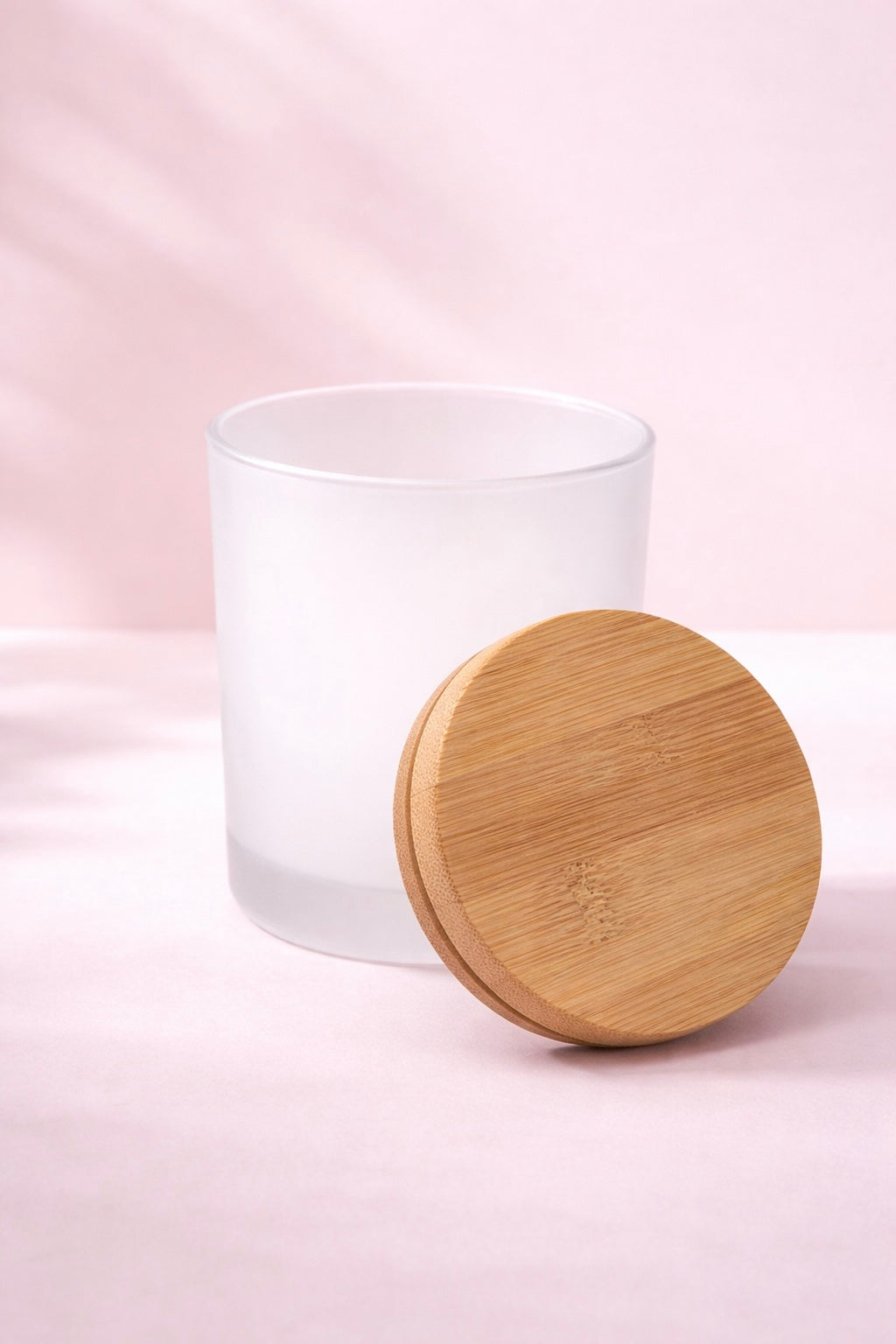 Frosted glass candle vessel with a wooden lid on a pink background