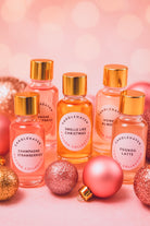 Best Christmas Fragrance Oils Canada | Set of small bottles with gold caps and 'Candle Haven' labels on a pink background with Christmas ornaments.
