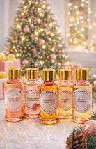Five small bottles of candle making fragrance oil with gold caps on a decorative surface with a Christmas tree in the background.