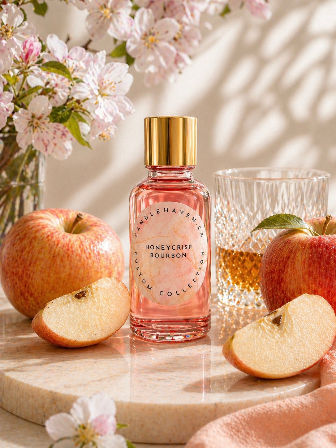 Pink glass bottle of honeycrisp bourbon fragrance oil for candle making by candlehaven.ca on a light background with apples, blossoms and a glass of bourbon.