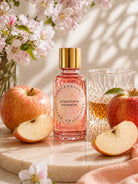 Pink glass bottle of honeycrisp bourbon fragrance oil for candle making by candlehaven.ca on a light background with apples, blossoms and a glass of bourbon.