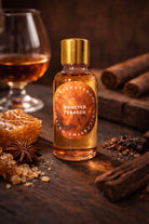 Bottle of 'Honeyed Tobacco’ candle fragrance oil on a wooden surface with cinnamon sticks and honeycomb.